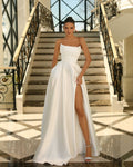 Woman in a white strapless gown with a high slit standing on a staircase.