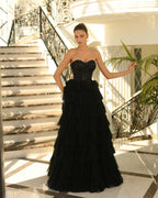 Woman in a black strapless gown standing in a sunlit room with marble floor and staircase.