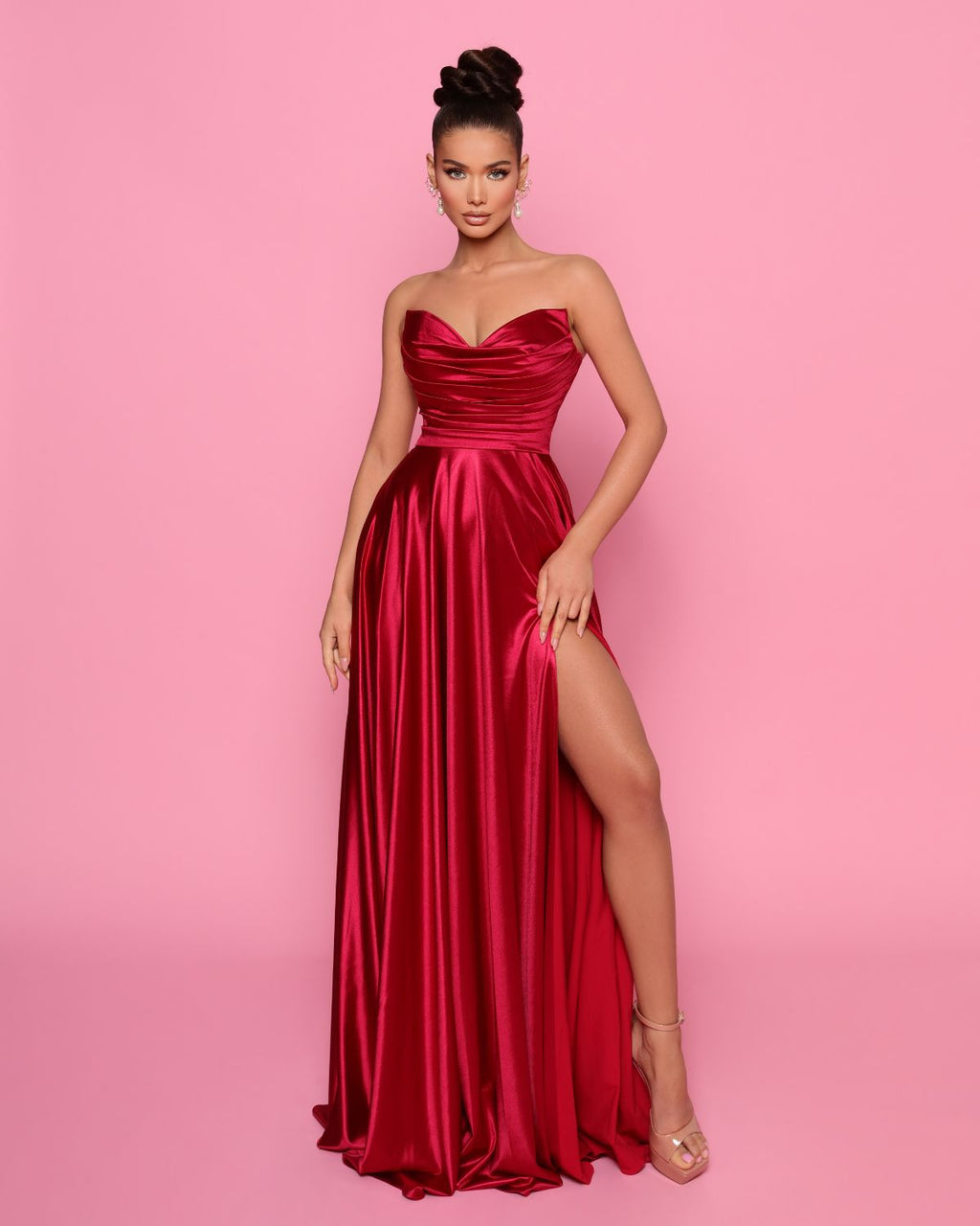 Woman wearing a red strapless gown with a high slit on a pink background
