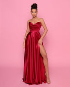 Woman wearing a red strapless gown with a high slit on a pink background