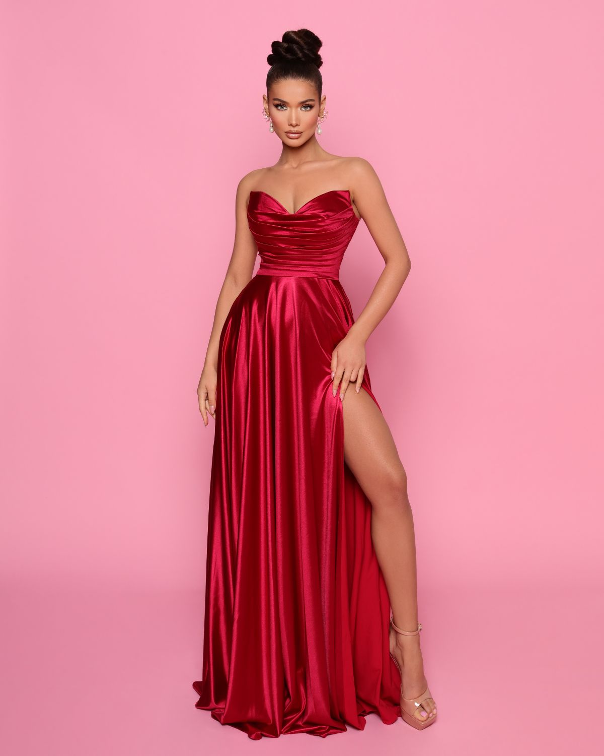 Woman wearing a red strapless gown with a high slit on a pink background