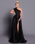 Woman wearing a black one-shoulder gown with a slit on a gray background