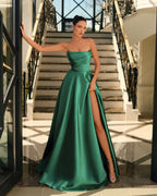 Woman in a green strapless gown with a high slit standing on a staircase.