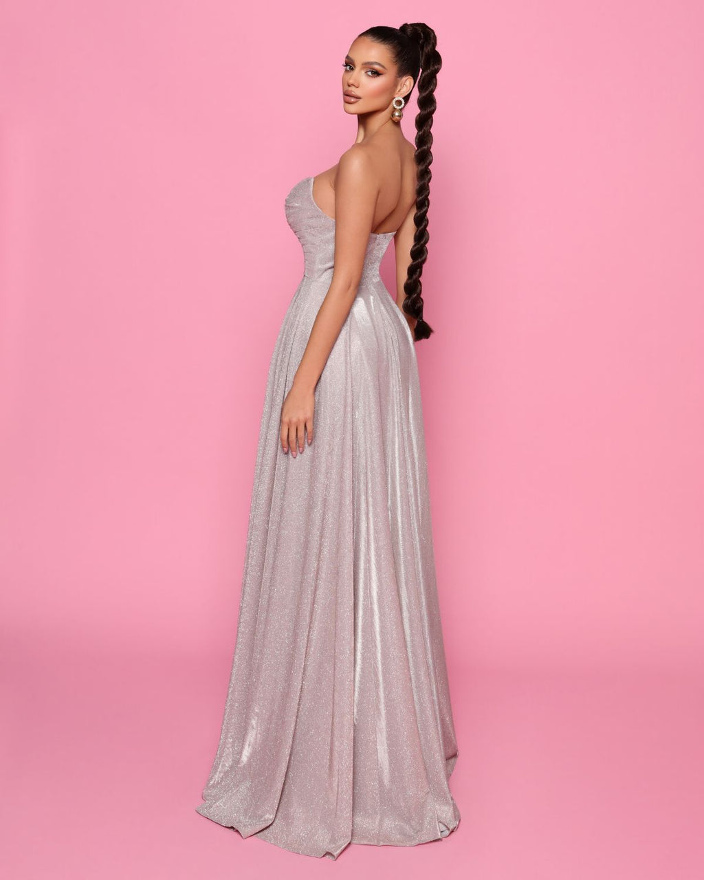 Woman in a silver evening gown against a pink background
