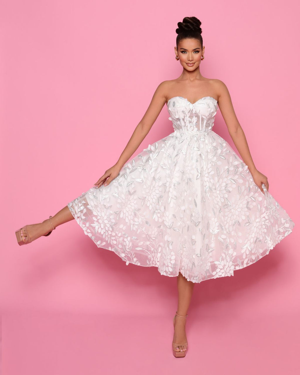 Woman wearing a white strapless dress against a pink background