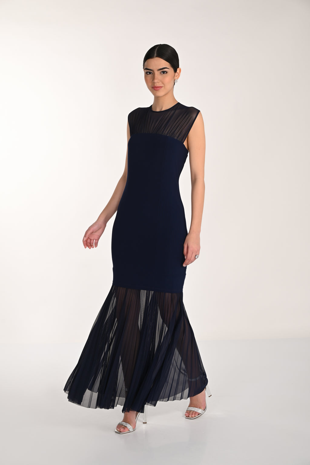 Woman wearing a navy blue dress with sheer black overlay on a white background