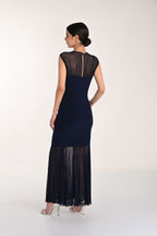 Woman wearing a navy dress with sheer black details on a white background