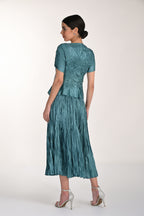 Woman wearing a teal dress with a textured skirt on a white background