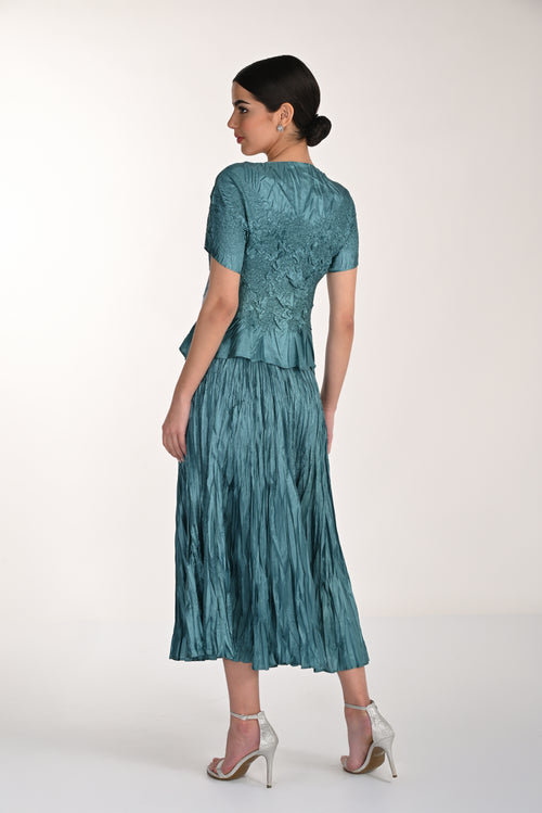 Woman wearing a teal dress with a textured skirt on a white background