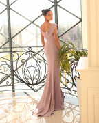 Woman in a pink evening gown standing in a room with large windows and decorative railing.