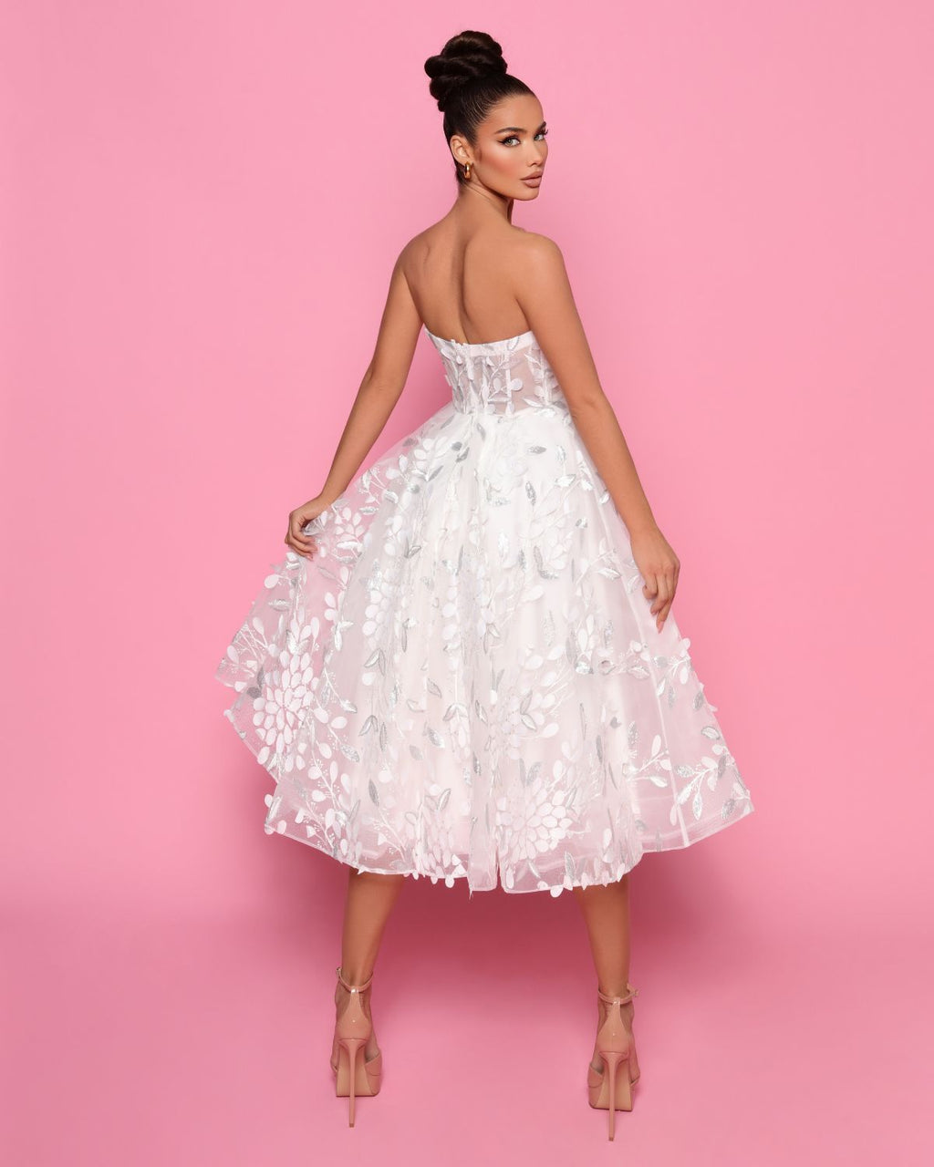 Woman wearing a white floral dress against a pink background