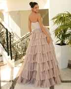 Woman in a strapless, tiered gown standing in an elegant interior setting.
