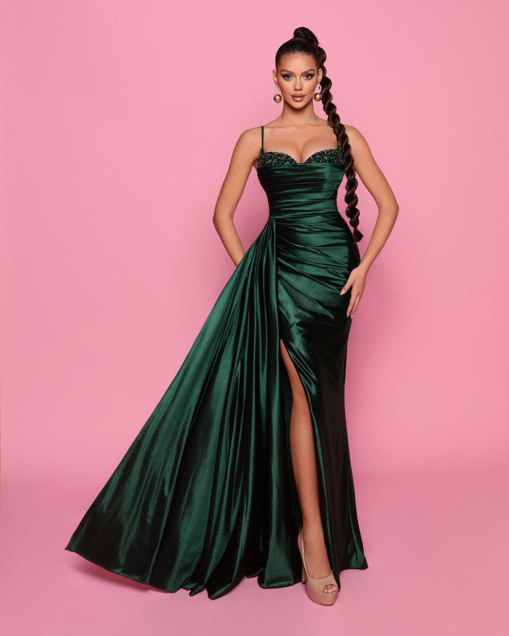 Woman wearing a green evening gown with a high slit on a pink background