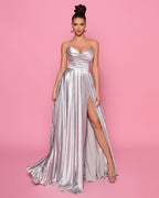 Woman wearing a silver strapless gown with a high slit on a pink background
