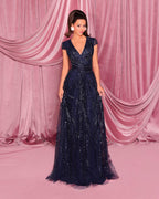 Woman in a navy blue evening gown against a pink curtain backdrop