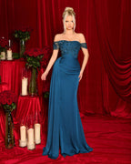 Woman in a blue evening gown standing against a red curtain backdrop.