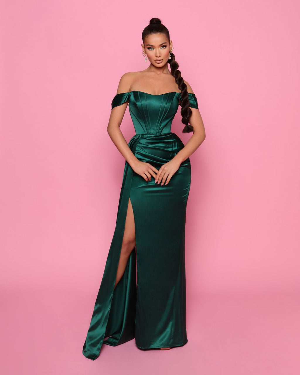 Woman wearing a green off-shoulder gown with a high slit on a pink background