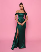 Woman wearing a green off-shoulder gown with a high slit on a pink background