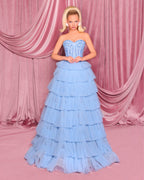 Woman in a light blue strapless gown with ruffled layers against a pink curtain backdrop