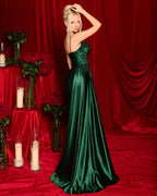 Woman in a green evening gown standing in front of red curtains with floral arrangements and candles on a table.