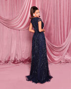Woman in a dark blue sequin gown standing against a pink draped curtain backdrop