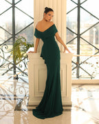Woman in a dark green evening gown standing in an elegant interior setting.