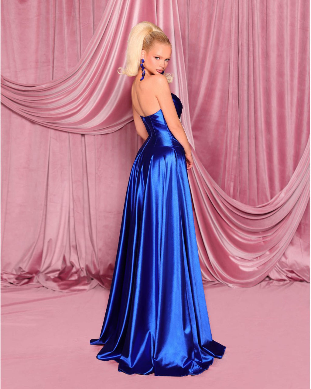 Woman in a blue evening gown standing against a pink curtain backdrop