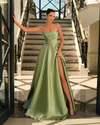 Woman in a green strapless gown with a high slit standing in an elegant interior setting.