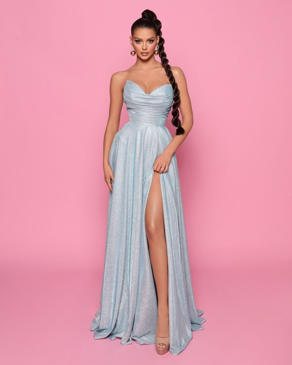 Woman in a light blue evening gown with a high slit on a pink background