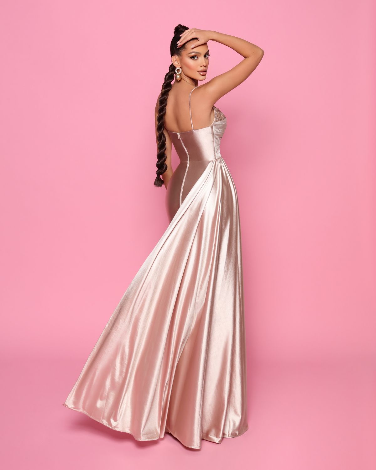 Woman in a long, light-colored satin dress against a pink background
