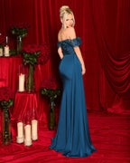 Woman in a blue evening gown standing in front of red curtains with floral arrangements and candles on a table.