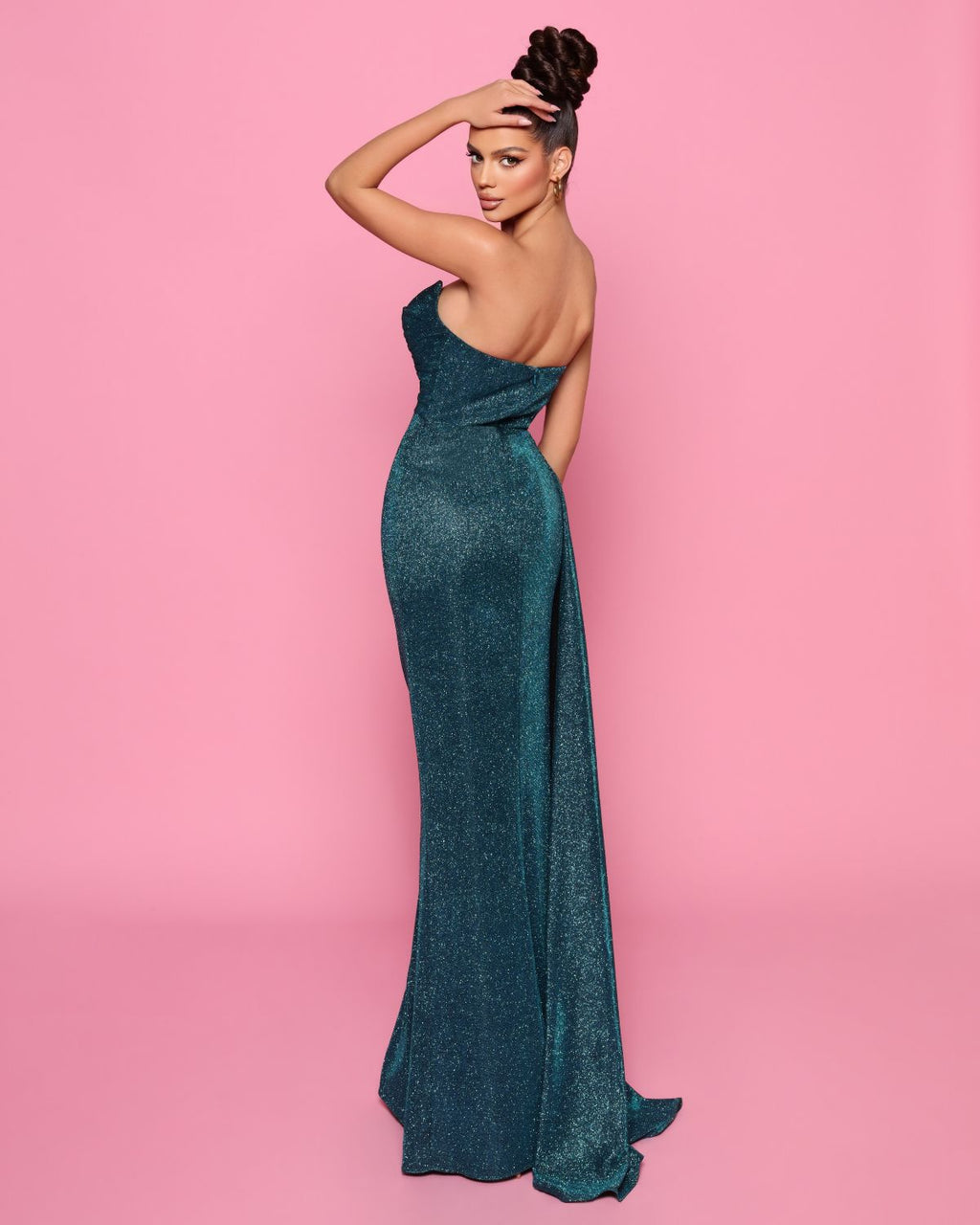 Woman in a teal strapless gown against a pink background
