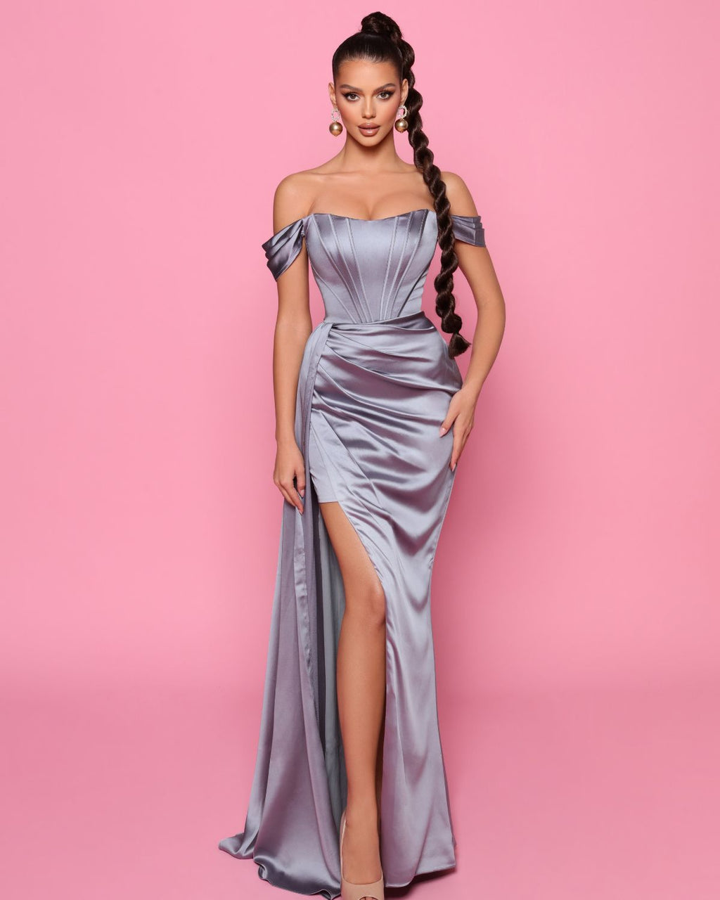 Woman wearing a silver off-shoulder gown with a high slit on a pink background