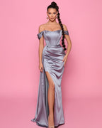 Woman wearing a silver off-shoulder gown with a high slit on a pink background