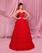Woman wearing a red strapless gown with layered skirt against pink curtains