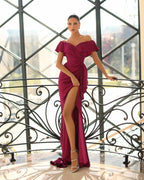 Woman in a burgundy off-shoulder gown with a high slit standing in front of decorative metal railings.