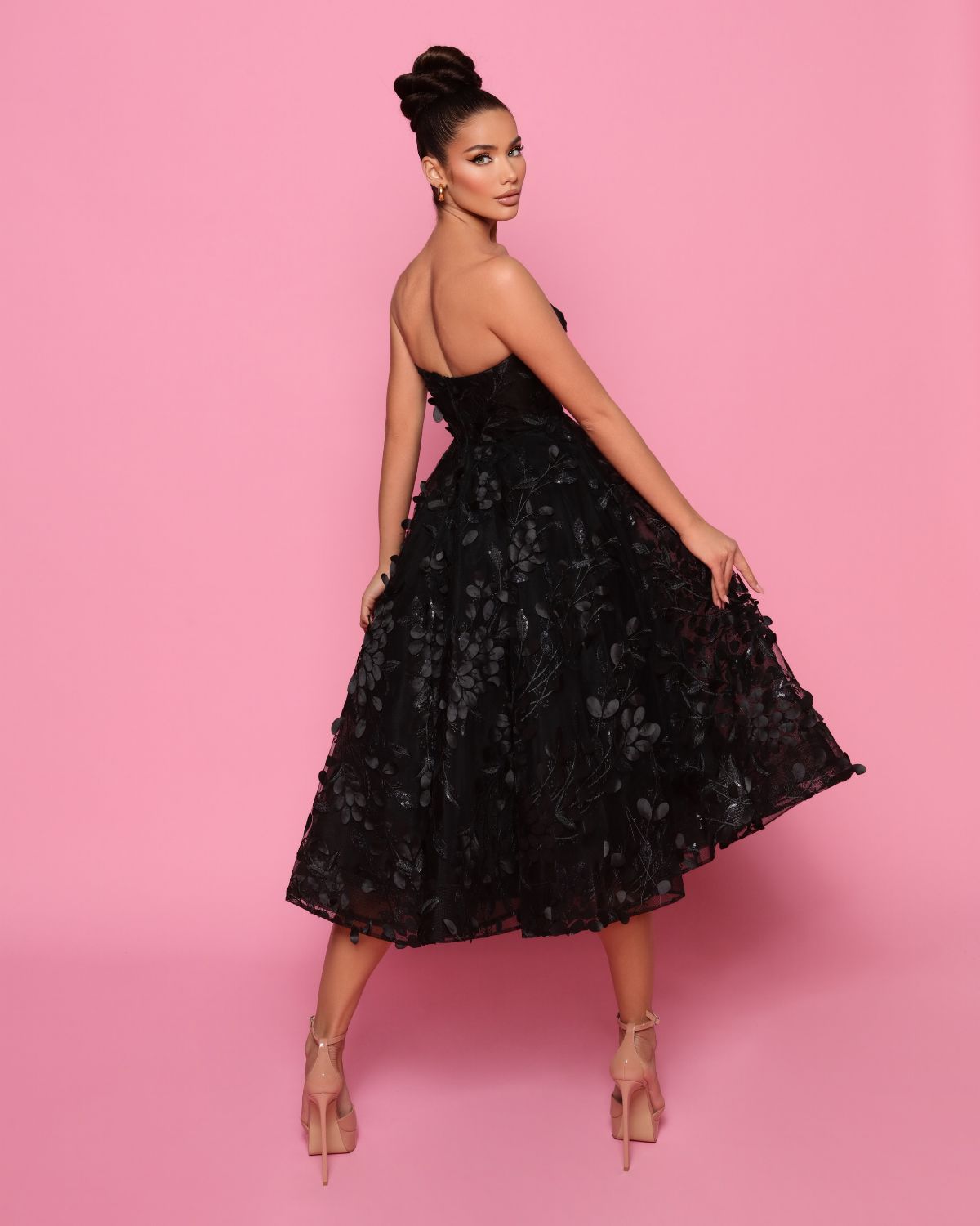 Woman wearing a black floral dress against a pink background
