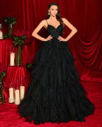 Woman in a black ruffled gown standing in front of a red curtain with floral decorations.