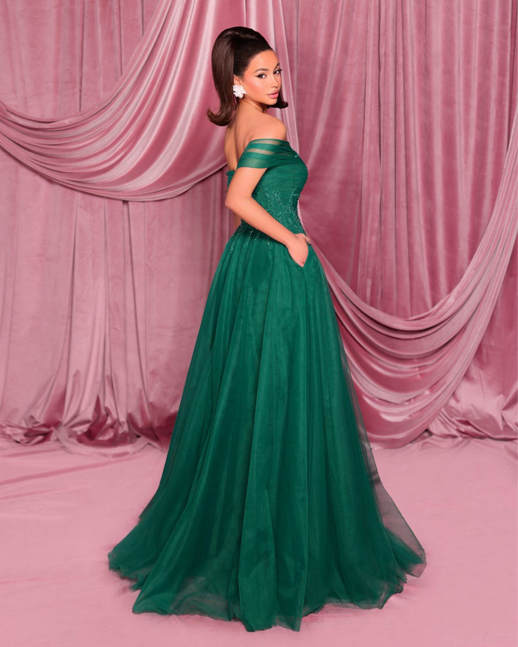 Woman in a green evening gown standing against a pink curtain backdrop
