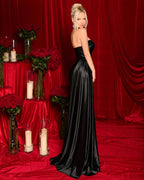 Woman in a black evening gown standing in front of a red curtain with floral arrangements and candles.
