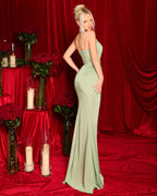 Woman in a green evening gown standing against a red curtain backdrop with floral arrangements and candles.
