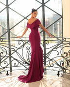 Woman in a burgundy evening gown standing in an elegant interior setting.