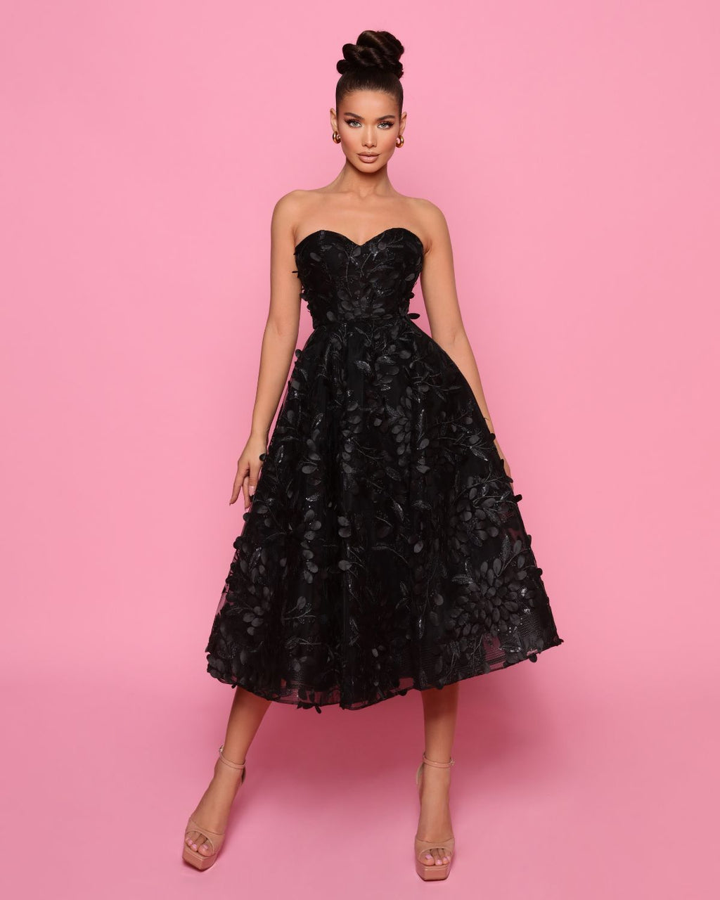 Woman wearing a black strapless dress with floral details on a pink background