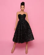 Woman wearing a black strapless dress with floral details on a pink background