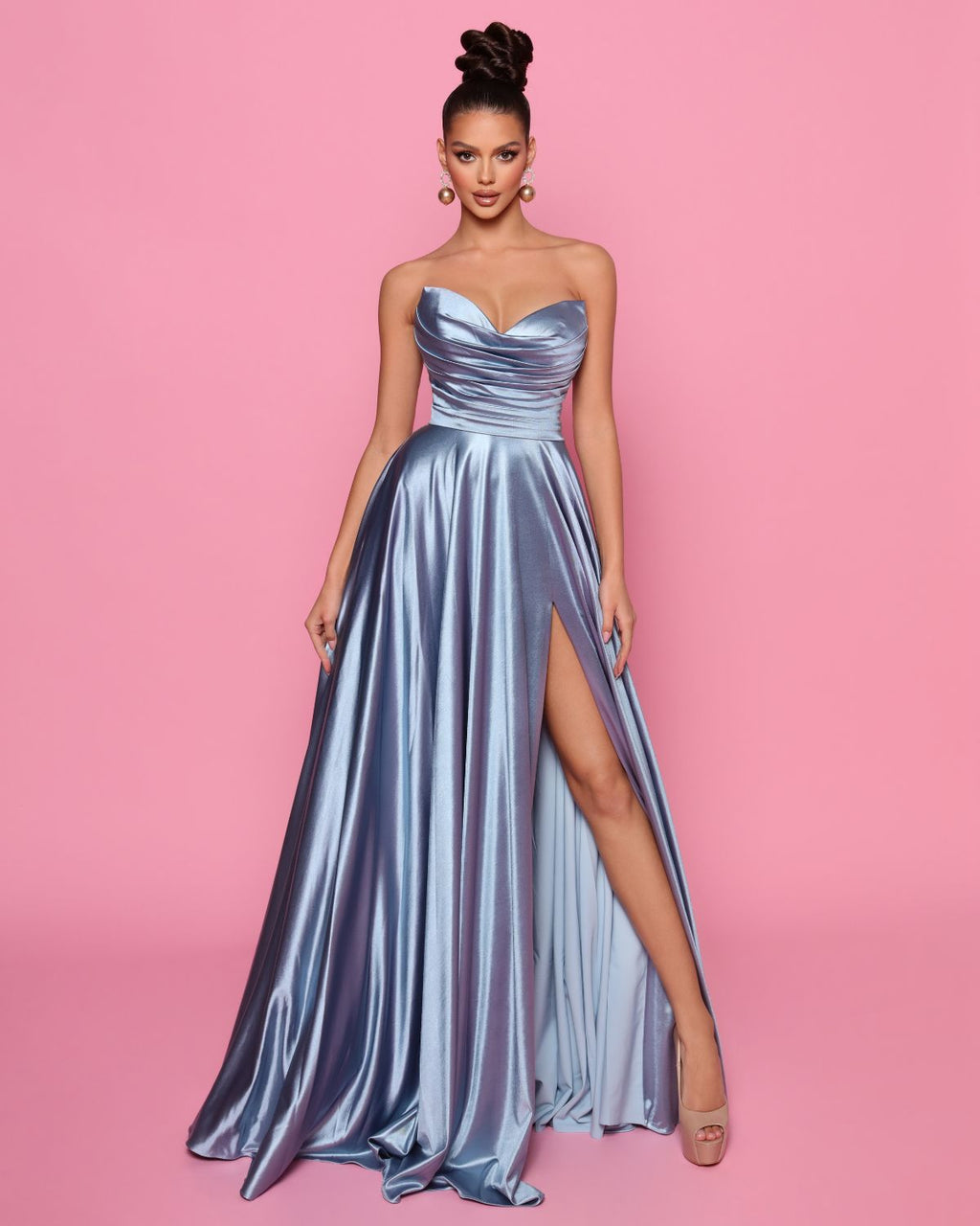 Woman wearing a strapless metallic gown with a high slit on a pink background