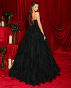 Woman in a black evening gown standing in front of red curtains and floral arrangements.