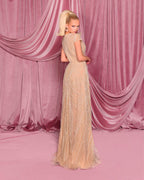 Woman in a beige evening gown standing in front of pink draped curtains.