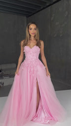 Woman wearing a pink evening gown with floral details and a high slit on a plain background