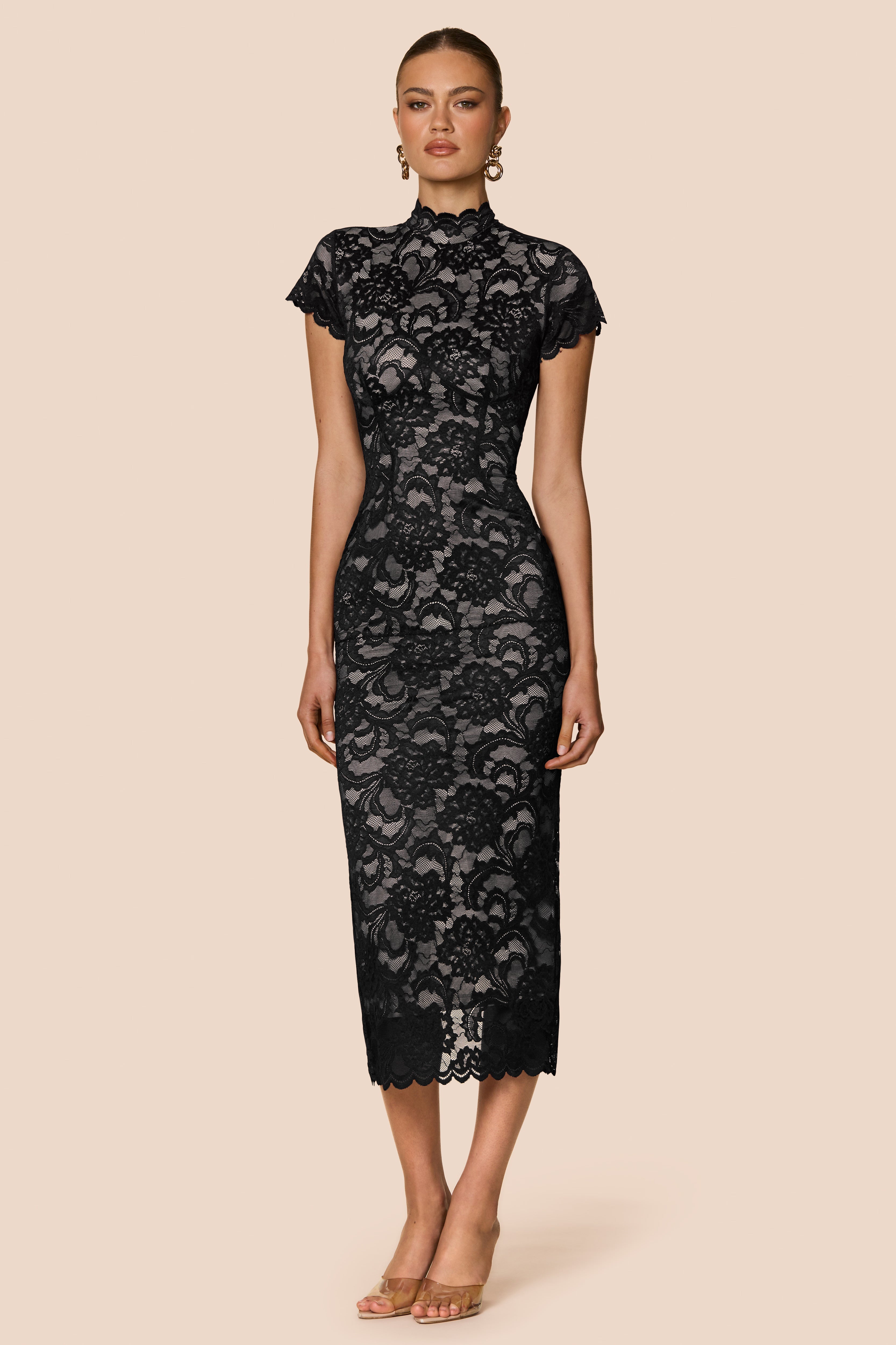 Black lace dress worn by a model on a beige background