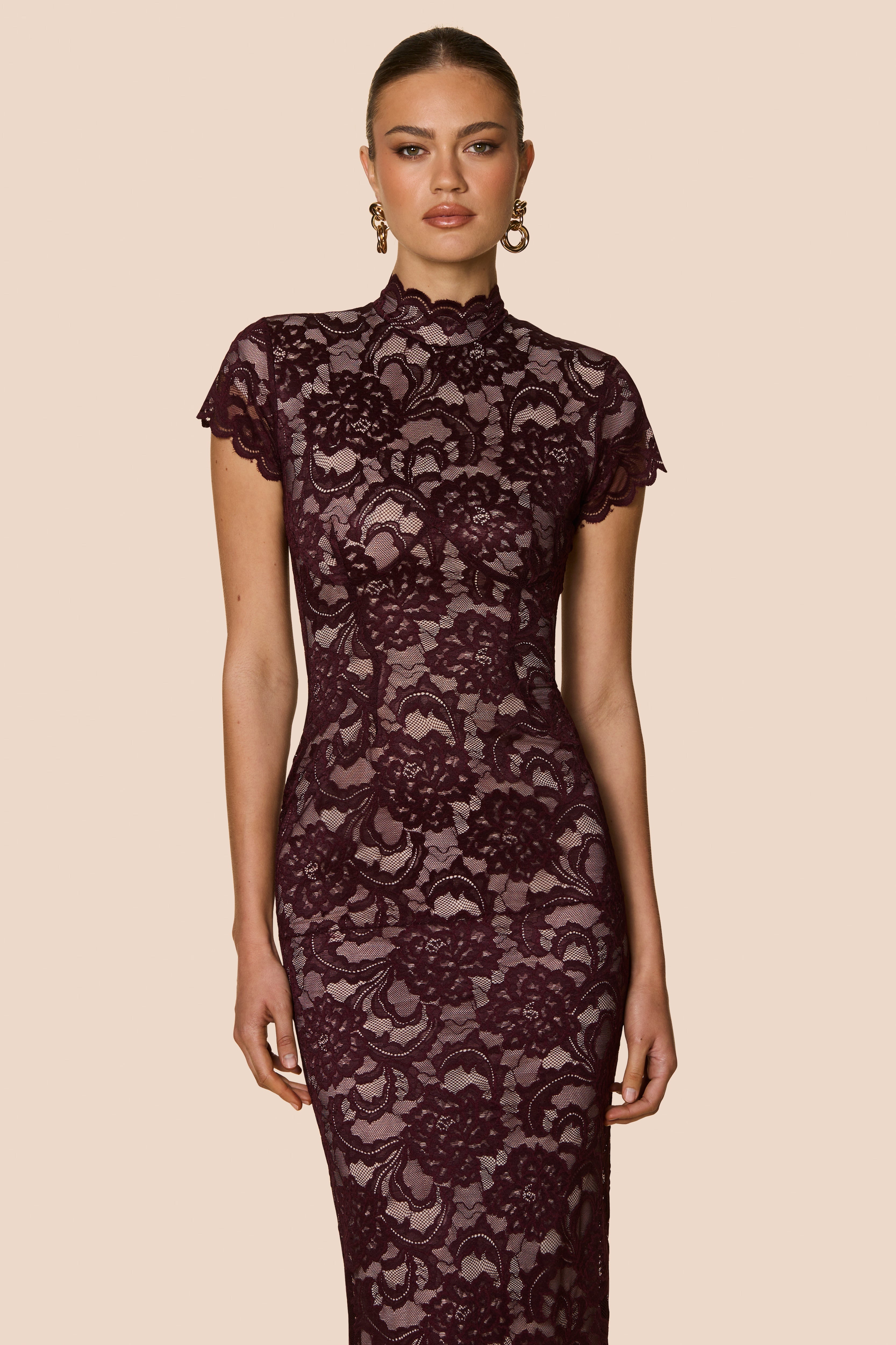 Woman wearing a dark lace dress against a beige background